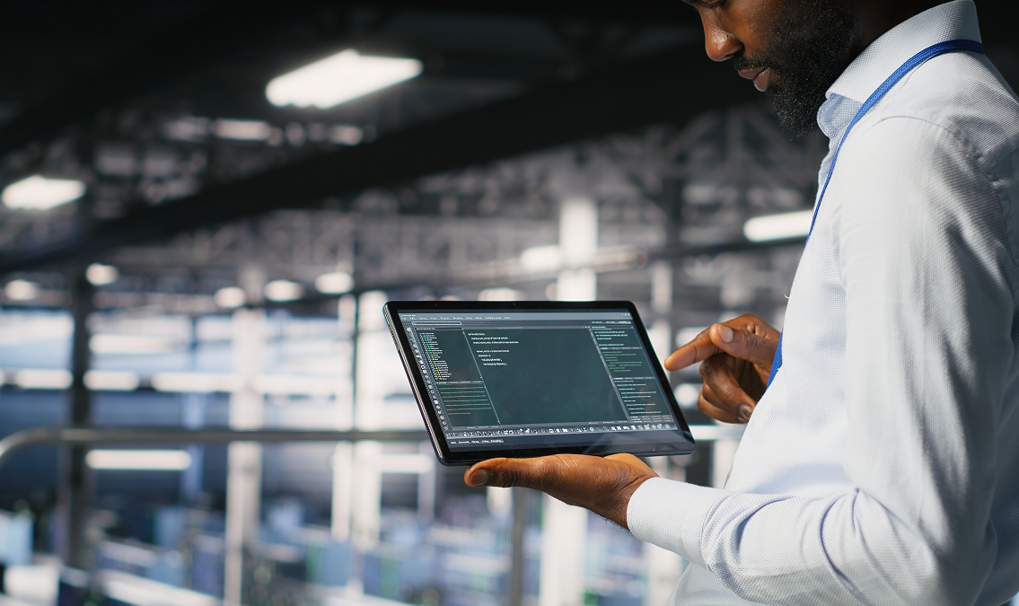 Business professional using a tablet to monitor AI-powered asset tracking and maintenance data inside an industrial facility